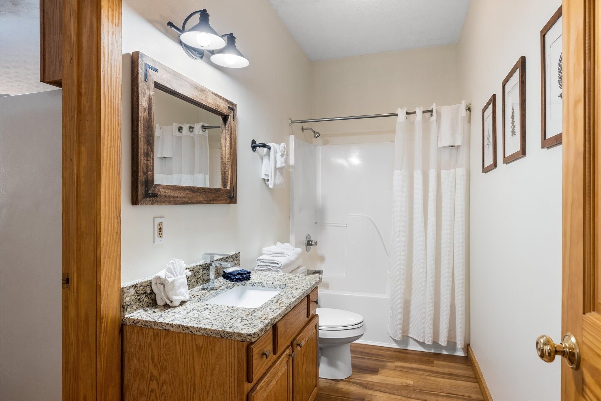 A bathroom with a wooden vanity, a sink, a mirror, a toilet, and a shower with a curtain.