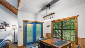 A dining area with a wooden table and chairs, a blue door, and a window with a view of trees. - Whitetail Cabin 2 Bedroom Cabin by RedAwning (Gatlinburg)
