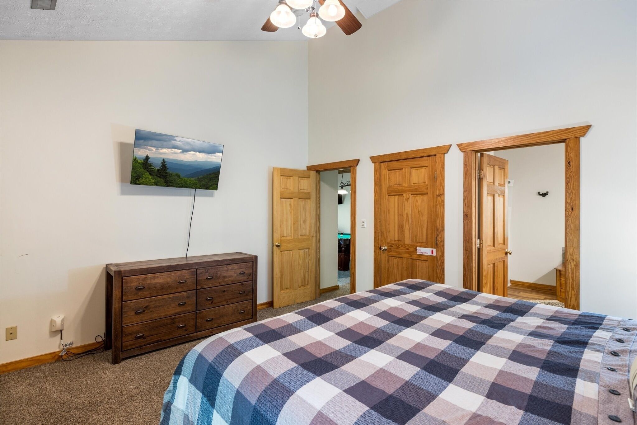 A bedroom with a large bed, a dresser, a painting on the wall, and wooden doors.