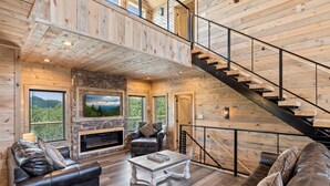 A spacious living area with a fireplace, leather sofas, and a staircase. - Red Sky Ridge 5 Bedroom Cabin by RedAwning (Sevierville)