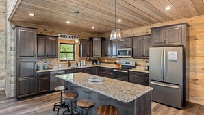 A modern kitchen with granite countertops, stainless steel appliances, and wooden cabinetry. - Red Sky Ridge 5 Bedroom Cabin by RedAwning (Sevierville)