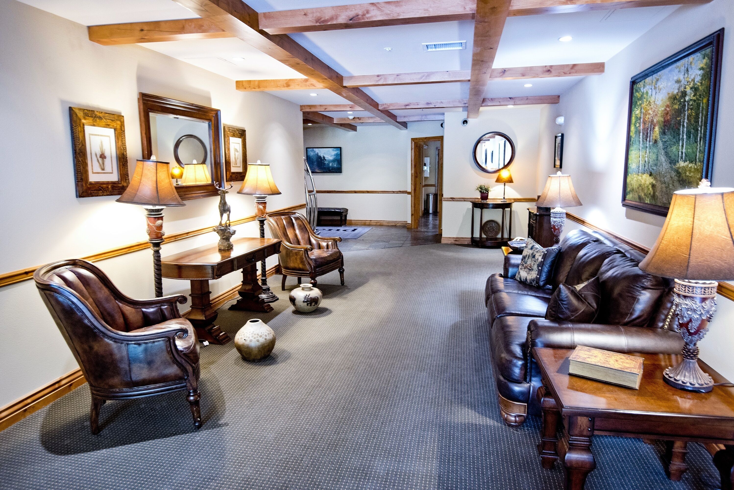 A spacious living room with leather furniture, wooden beams, and framed artwork on the walls.
