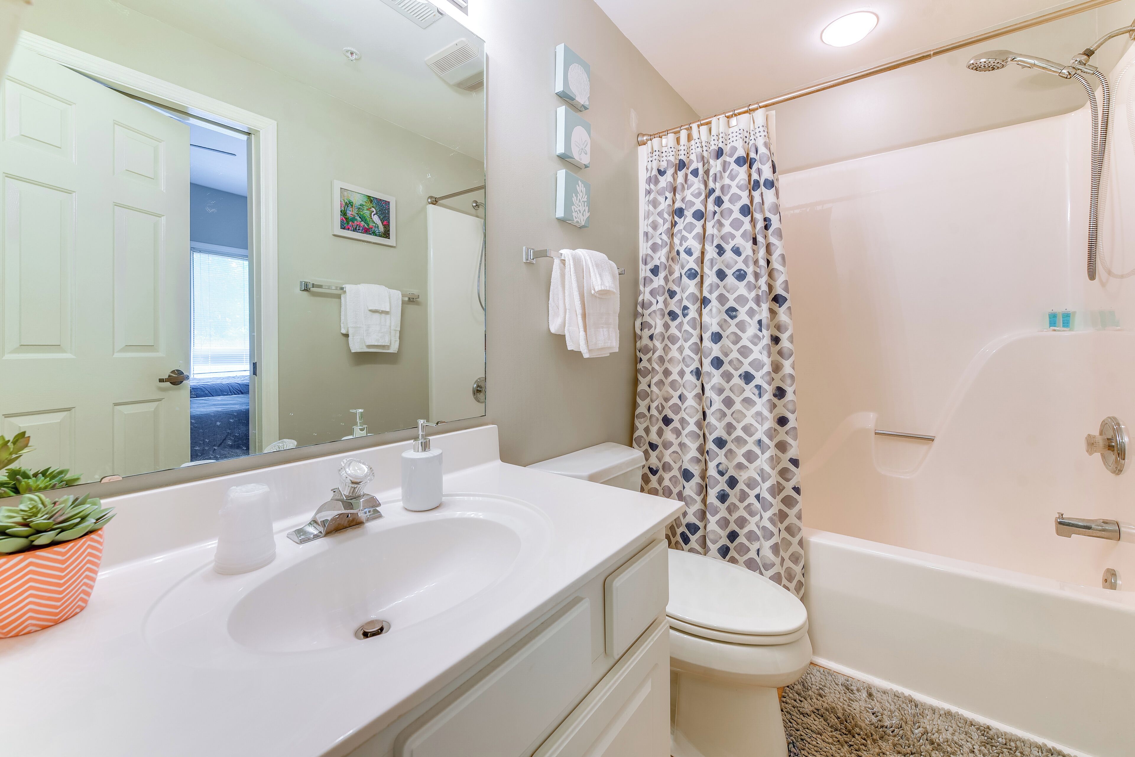 A bathroom with a white sink, toilet, and bathtub. There is a shower curtain with a geometric pattern, and a potted plant on the sink.