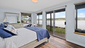 Un dormitorio con una cama grande, un escritorio y vistas a un lago a través de puertas corredizas de vidrio.