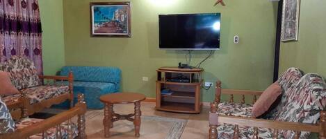 A living room with a sofa, two chairs, a coffee table, a TV, and a painting on the wall.