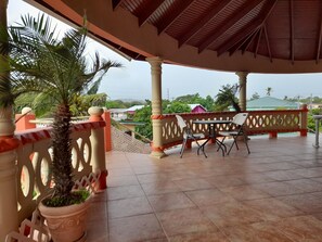 A covered outdoor area with a tiled floor, a table with chairs, and a potted plant. - Islanders Place (Canaan)