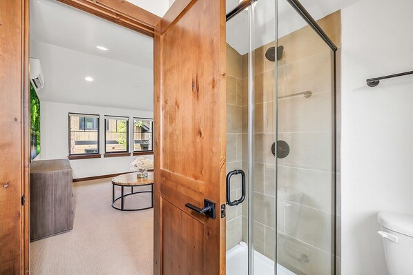 Un baño moderno con cabina de ducha de vidrio, puerta de madera y un inodoro a la vista.
