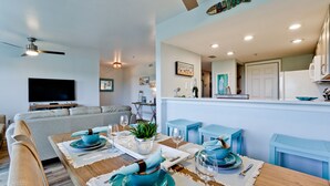 Una sala de estar moderna con un sofá, una mesa de comedor para cuatro personas y una cocina con refrigerador y armarios.
