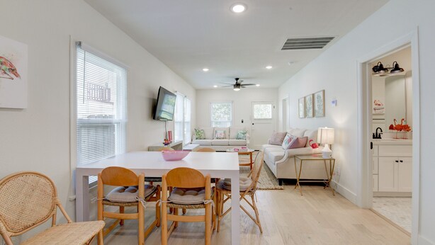 Un salón amplio con una mesa de comedor, sillas, un sofá y un televisor montado en la pared.
