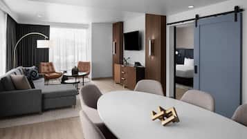 Una habitación de hotel moderna con sofá, sillas, una mesa de comedor, televisor y armario.