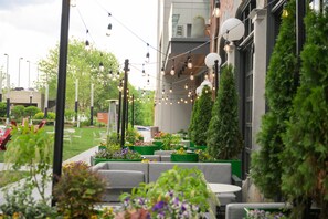 An outdoor seating area with green planters, grey sofas, and string lights. - Hotel West & Main Conshohocken Philadelphia, Tapestry Collection (Conshohocken)