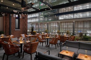 An indoor dining area with brick walls, modern lighting, and a view of the city through large windows. - Hotel West & Main Conshohocken Philadelphia, Tapestry Collection (Conshohocken)