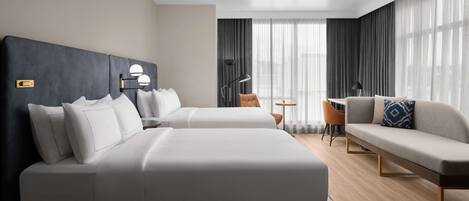 A modern hotel room with two beds, a sofa, a small table, and a chair.