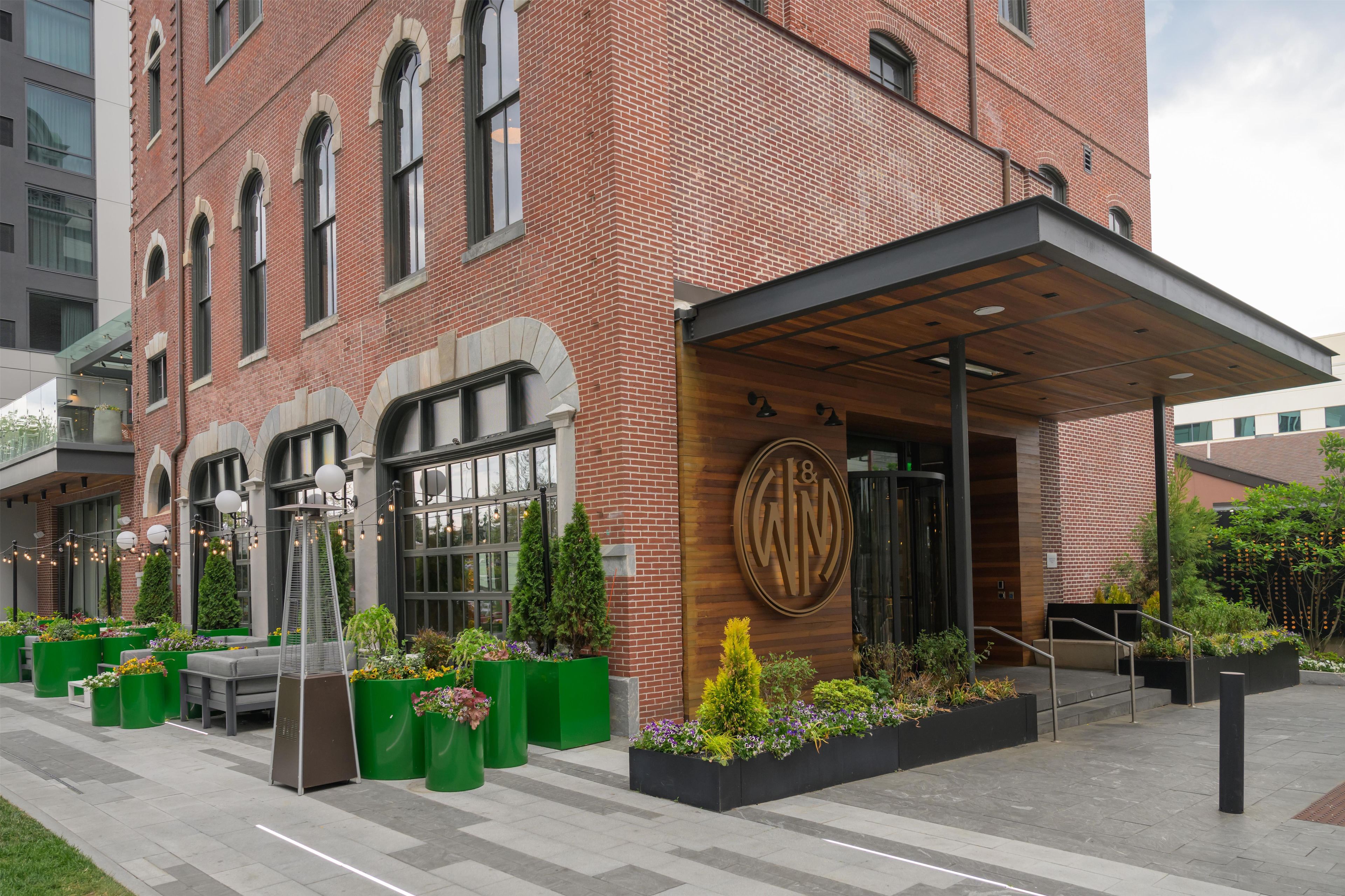 A brick building with a wooden entrance, outdoor seating, and green planters.