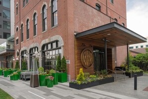 A brick building with a wooden entrance, outdoor seating, and green planters. - Hotel West & Main Conshohocken Philadelphia, Tapestry Collection (Conshohocken)