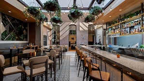 Un área de bar moderna con diversas opciones de asientos, una barra y plantas colgantes.