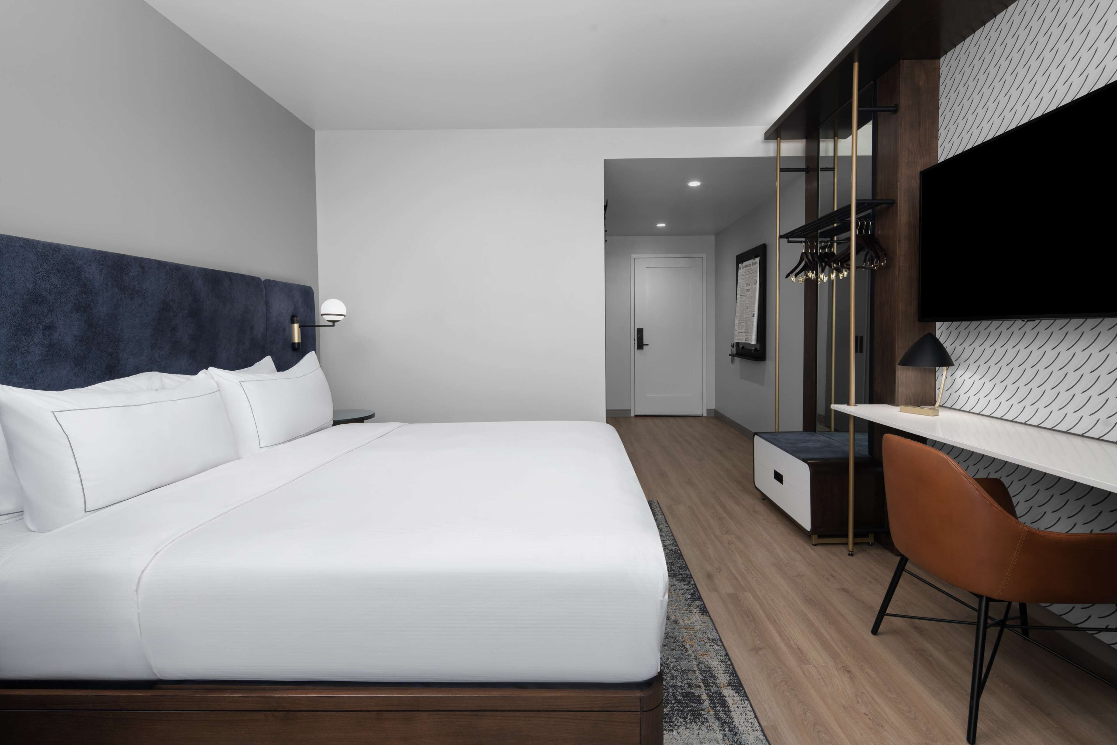 Une chambre d’hôtel moderne avec un grand lit, un bureau et un téléviseur fixé au mur.