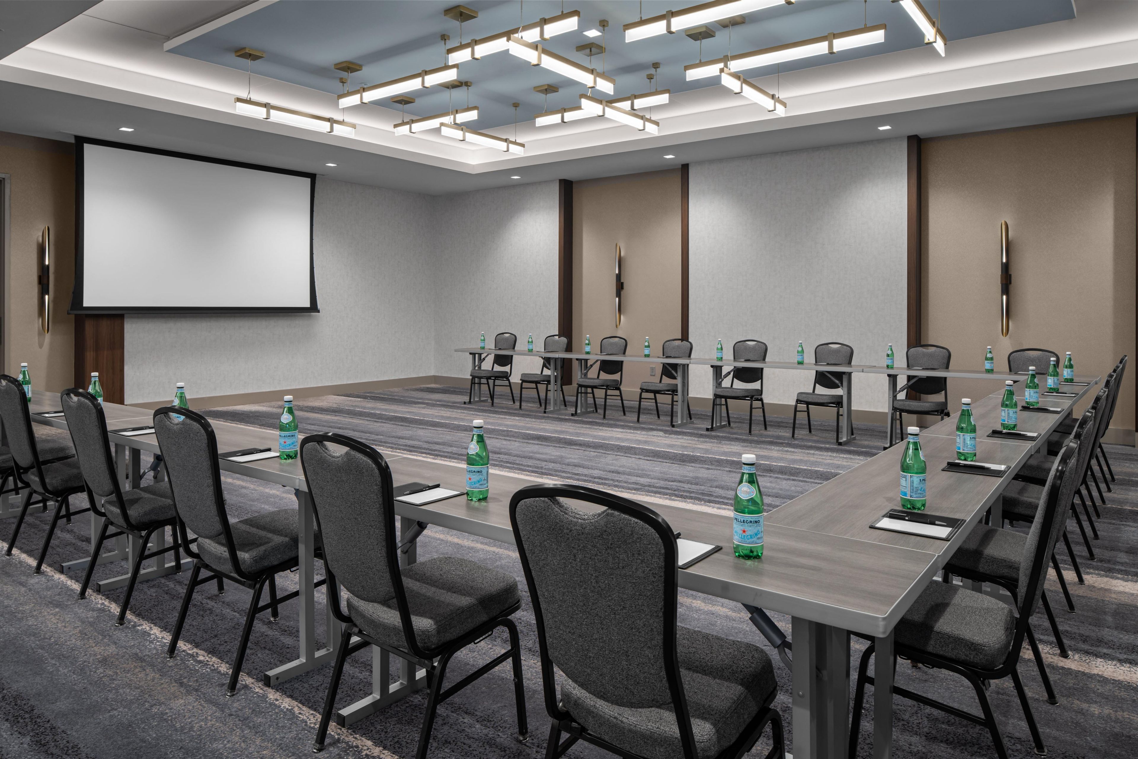 A conference room with a long table, chairs, a projector screen, and water bottles.