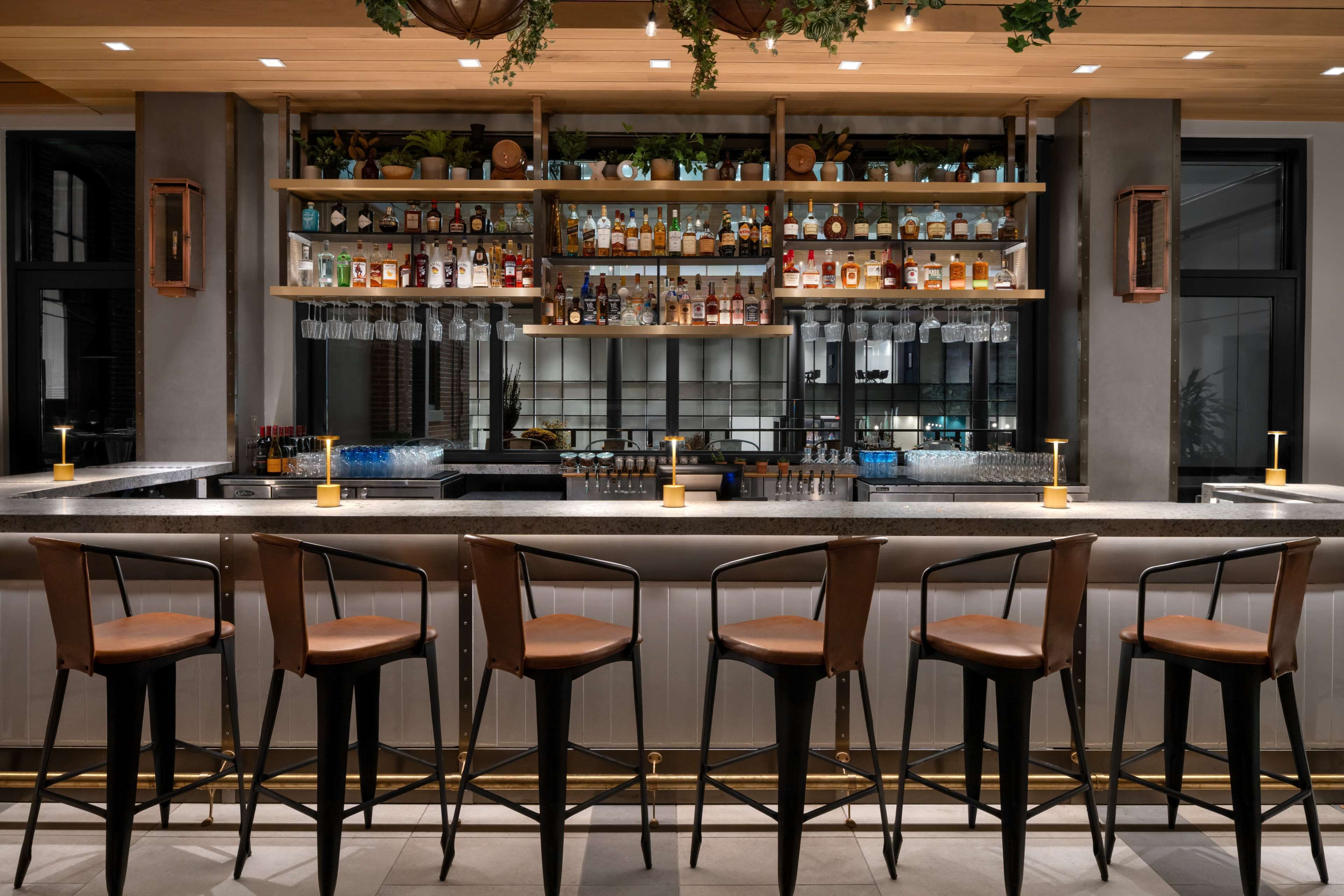 Eine Bar mit einer langen Theke, mehreren Flaschenregalen und vier Barhocker.