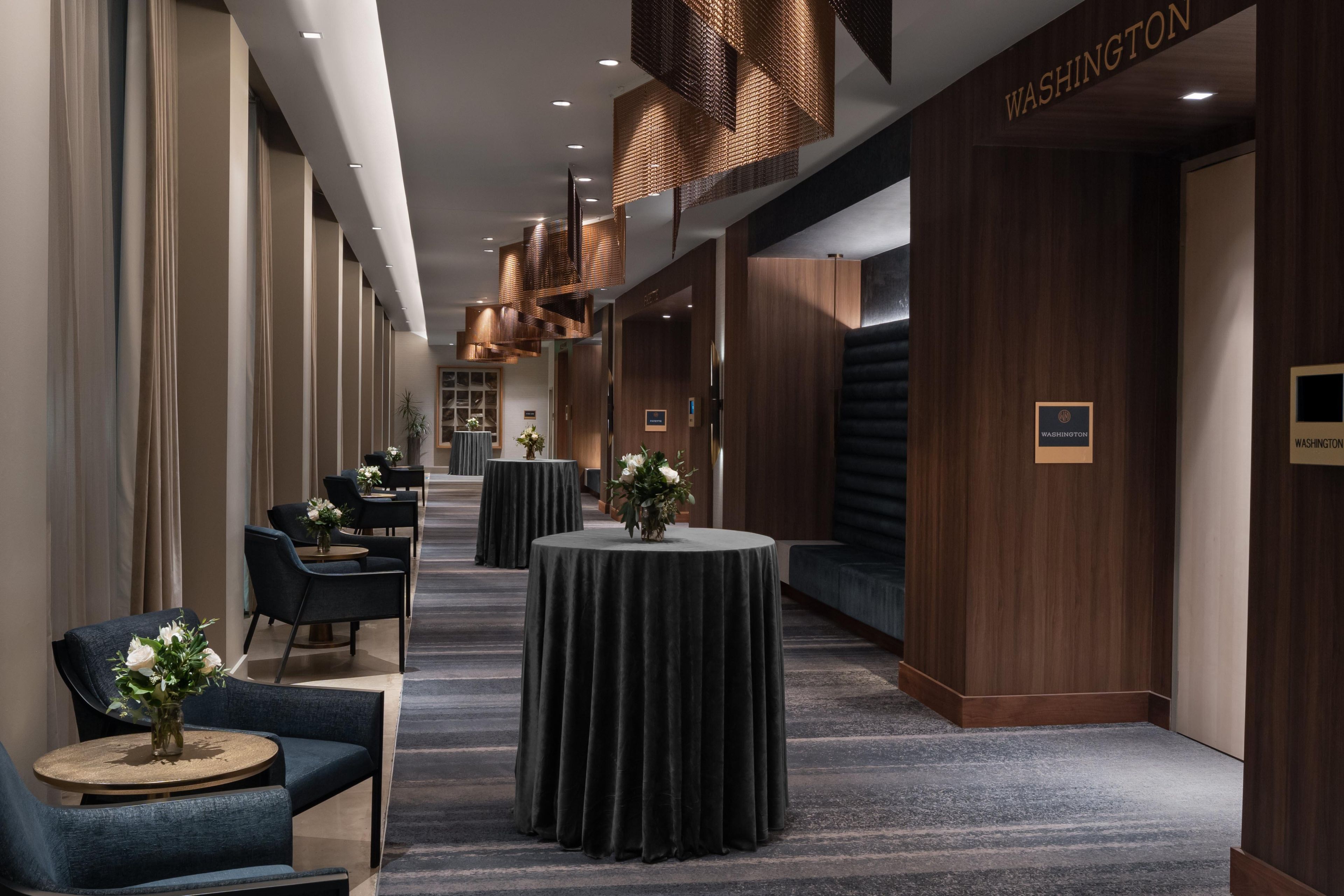 A hotel corridor with round tables, chairs, and a sign reading 'WASHINGTON'.