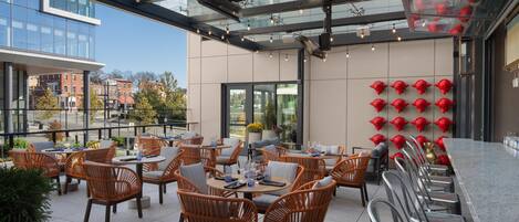 An outdoor seating area with wicker chairs and tables, a glass ceiling, and a row of red fire hydrants on the wall.