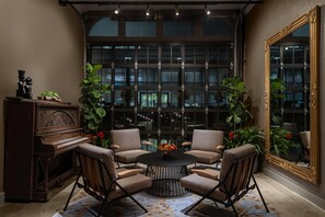 A room with a piano, two chairs, a round table, and a large mirror. - Hotel West & Main Conshohocken Philadelphia, Tapestry Collection (Conshohocken)