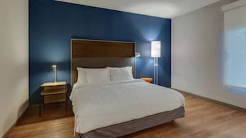 Una habitación de hotel moderna con una cama grande, suelo de madera y una pared de acento azul.