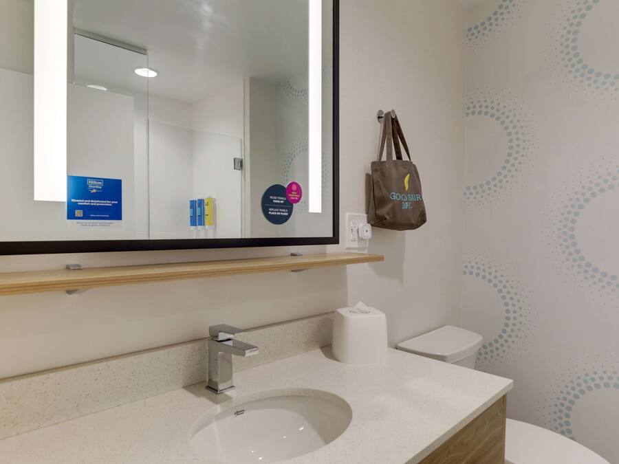 Un baño moderno con un espejo grande, un lavamanos, un inodoro y un dispensador de toallas.