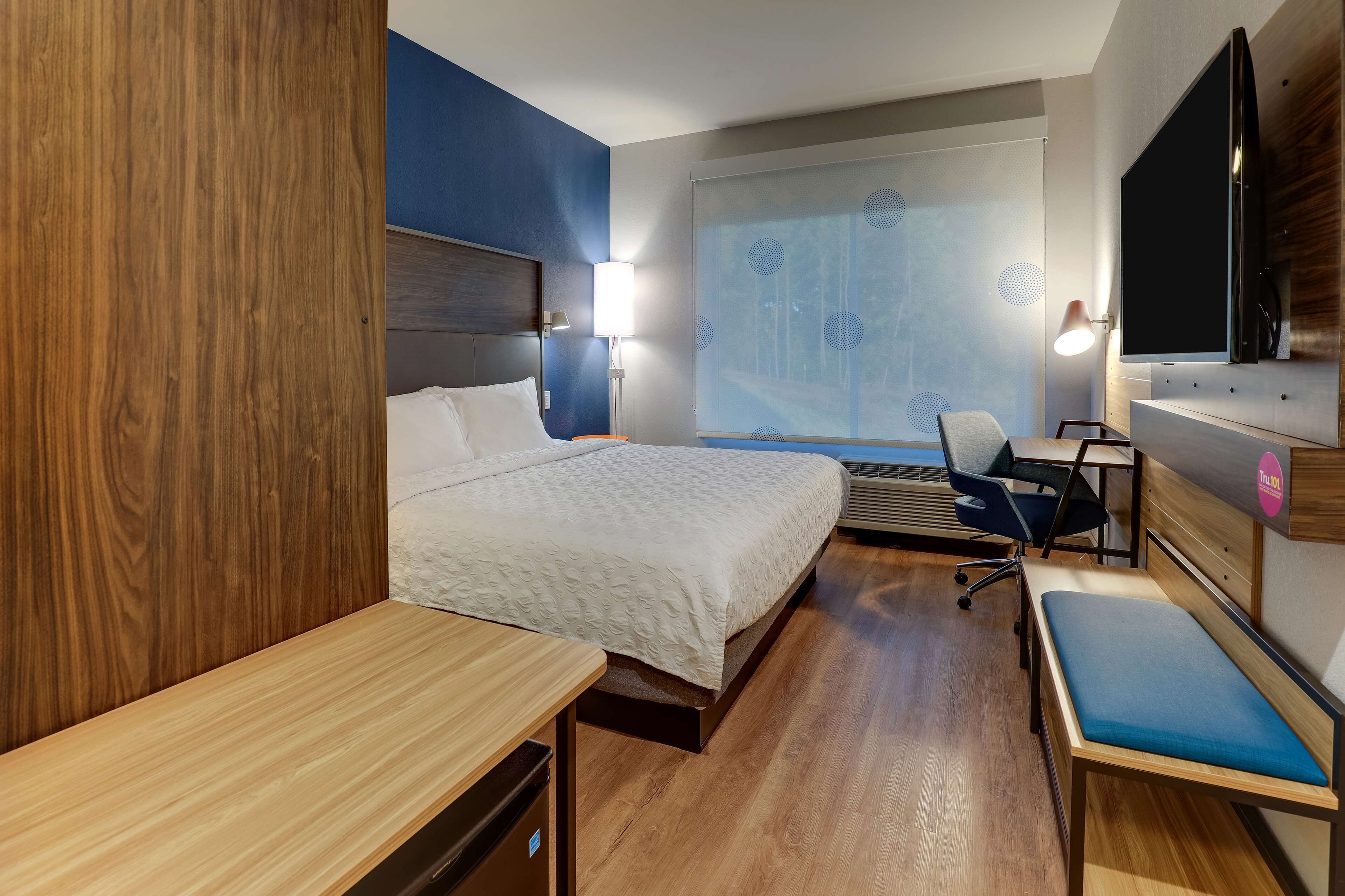 A hotel room with a bed, desk, chair, and a TV mounted on the wall.