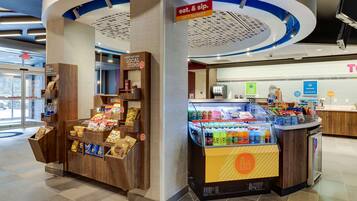 Zona comercial abierta las 24 horas con una variedad de bocadillos y bebidas, una sección de productos locales y una caja de pago.