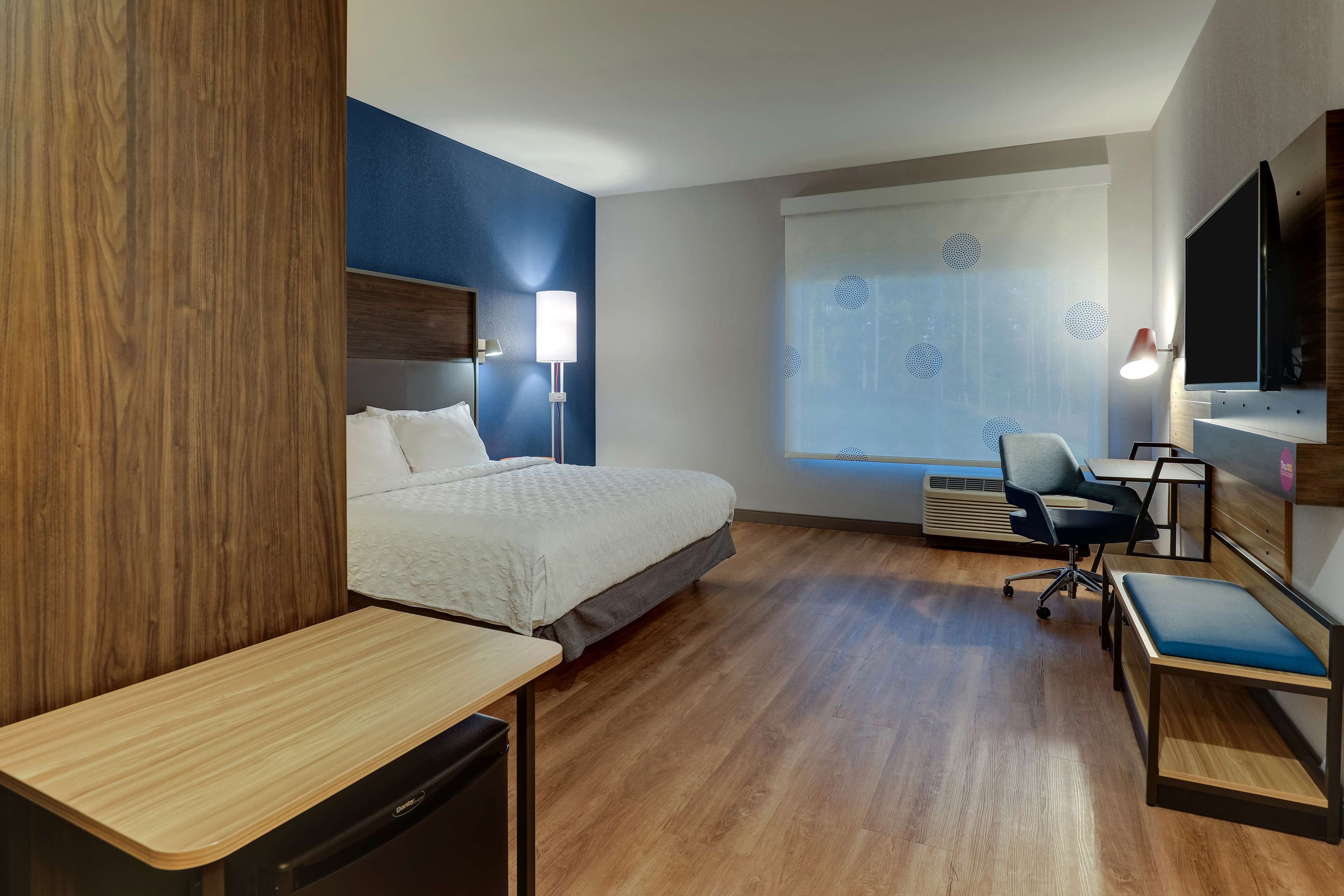 A hotel room with a bed, desk, chair, TV, and window with blinds.