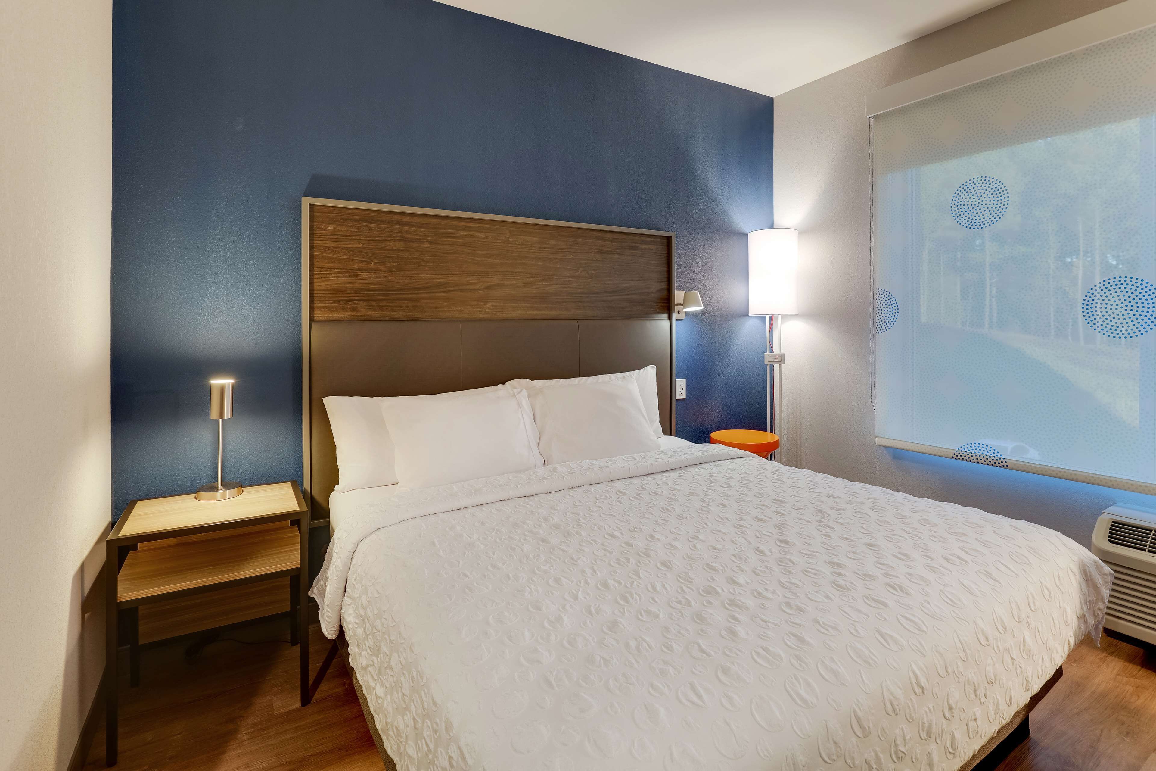 Une chambre d’hôtel avec un grand lit, une tête de lit en bois, deux tables de chevet et une fenêtre donnant sur des arbres.