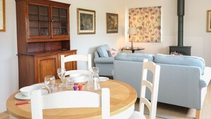 A cozy living room with a dining table set for four, a blue sofa, a wooden cabinet, and a fireplace. - Flagstone Cottage (Cheltenham)
