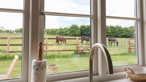 A bathroom with a large window, a wooden chair, a toilet paper holder, and a small decorative bowl. - Flagstone Cottage (Cheltenham)