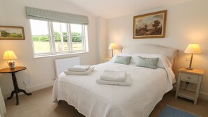 A neatly arranged bedroom with a large bed, two bedside tables, a window with a view, and a painting on the wall. - Flagstone Cottage (Cheltenham)