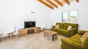 A modern living room with a wooden ceiling, a green sofa, a TV, and a white chair.