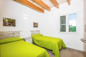 Camera da letto con due letti, travi in legno a vista al soffitto, una finestra con persiane e due quadri appesi al muro.