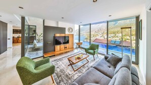 A modern living room with a large TV, comfortable seating, and a view of a mountainous landscape. - Villa Bank Two - Three Bedroom Villa, Sleeps 8 (Kalkan)