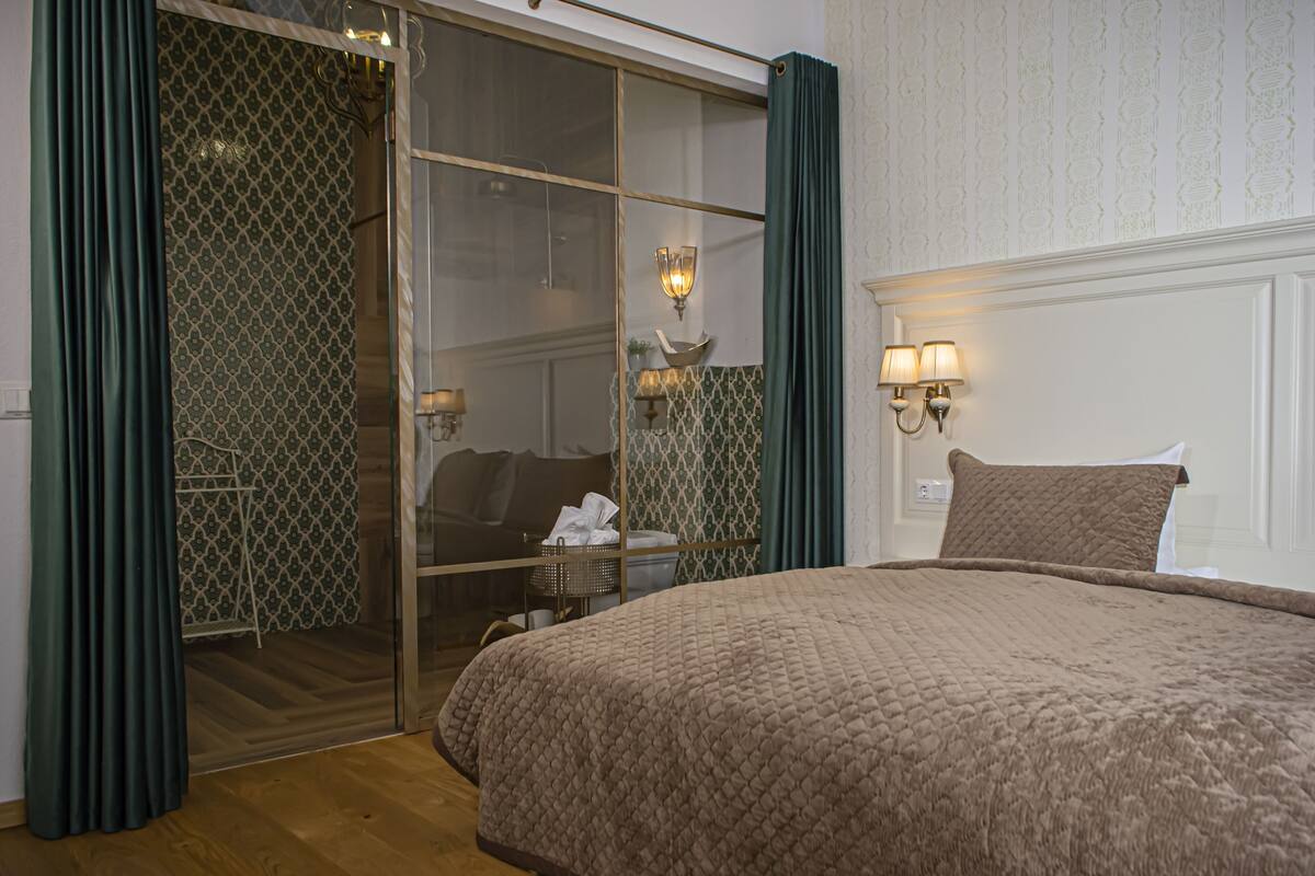 A hotel room with a large bed, a sliding glass door, a small table with a lamp, and a wall-mounted light fixture.