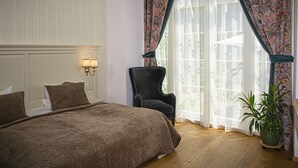 A bedroom with a large bed, a chair, a potted plant, and a window with curtains. - Palatul Brukenthal Avrig (Avrig)