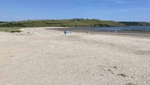 A beach with a sandy foreground, a blue structure, and rolling green hills in the background. - Luxury 2 Bedroom Holiday Home on Beachside Park (Par)