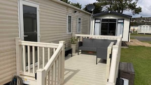 A mobile home with a deck, a small porch, and a satellite dish. - Luxury 2 Bedroom Holiday Home on Beachside Park (Par)