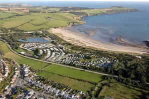 Luchtbeeld van een kustgebied met een groot stacaravancamp, een strand en omliggende velden.