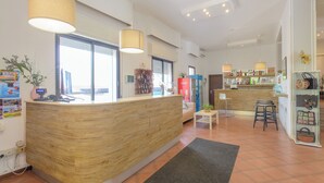 A reception desk with a wooden finish, a seating area with a small table and chairs, and a bar area with stools. - Hotel Avana Mare (Rimini)