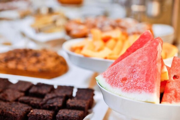 Un buffet proposant une variété de plats, notamment des tranches de pastèque, des brownies et d’autres desserts.