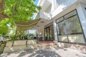 Un espacio de estar al aire libre cubierto con un patio, un coche estacionado cerca y un edificio con grandes ventanales.