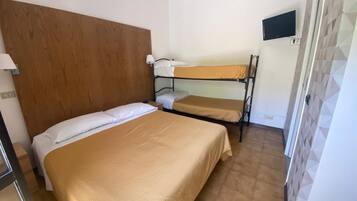Une chambre avec un lit simple, un lit superposé, une tête de lit en bois, un téléviseur fixé au mur et un sol carrelé.