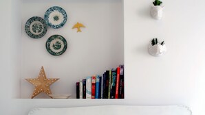 Una parete bianca decorata con piatti ornamentali, una stella e un piccolo uccello giallo, oltre a una libreria piena di libri.