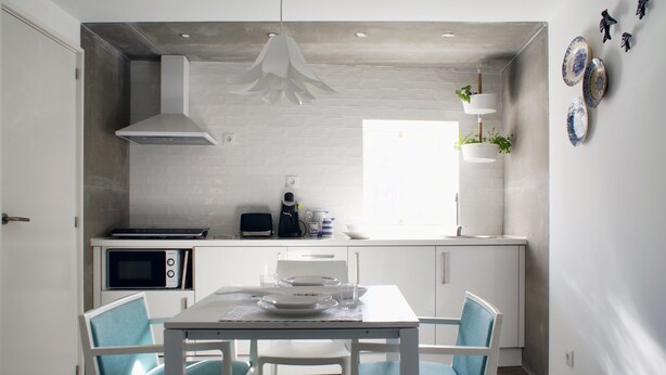 Una cucina compatta con mobili bianchi, un forno a microonde, un tostapane e un tavolo con sedie blu.