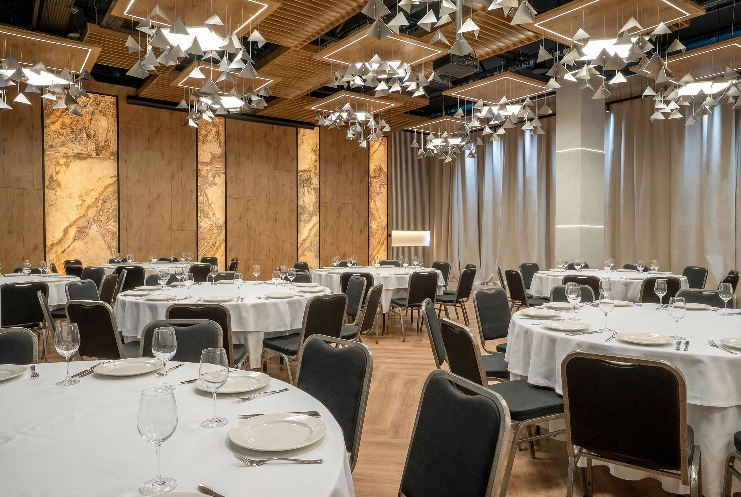 A banquet hall with round tables, white tablecloths, and hanging geometric light fixtures.